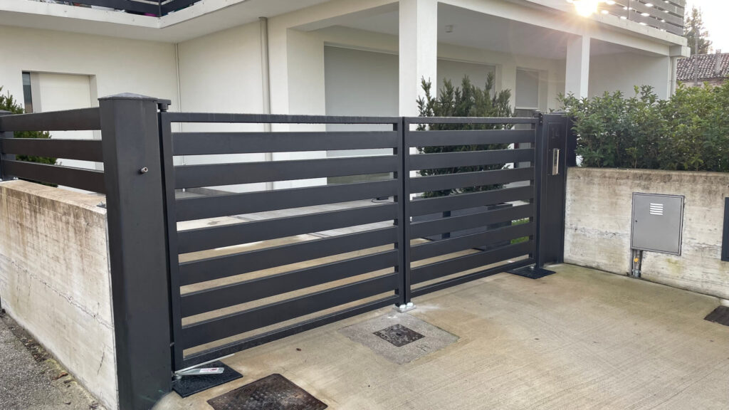Cancello carraio a due ante a battente in metallo nero, con un design moderno a fasce orizzontali abbinato alla recinzione perimetrale adiacente 2A Carpenteria