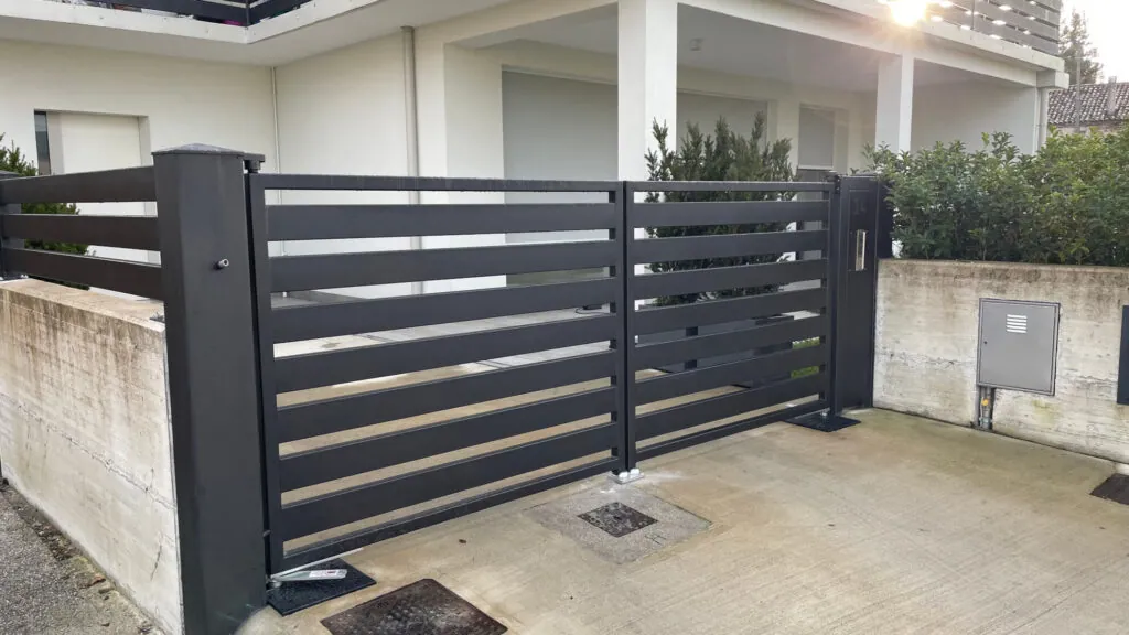 Cancello carraio a due ante a battente in metallo nero, con un design moderno a fasce orizzontali abbinato alla recinzione perimetrale adiacente 2A Carpenteria