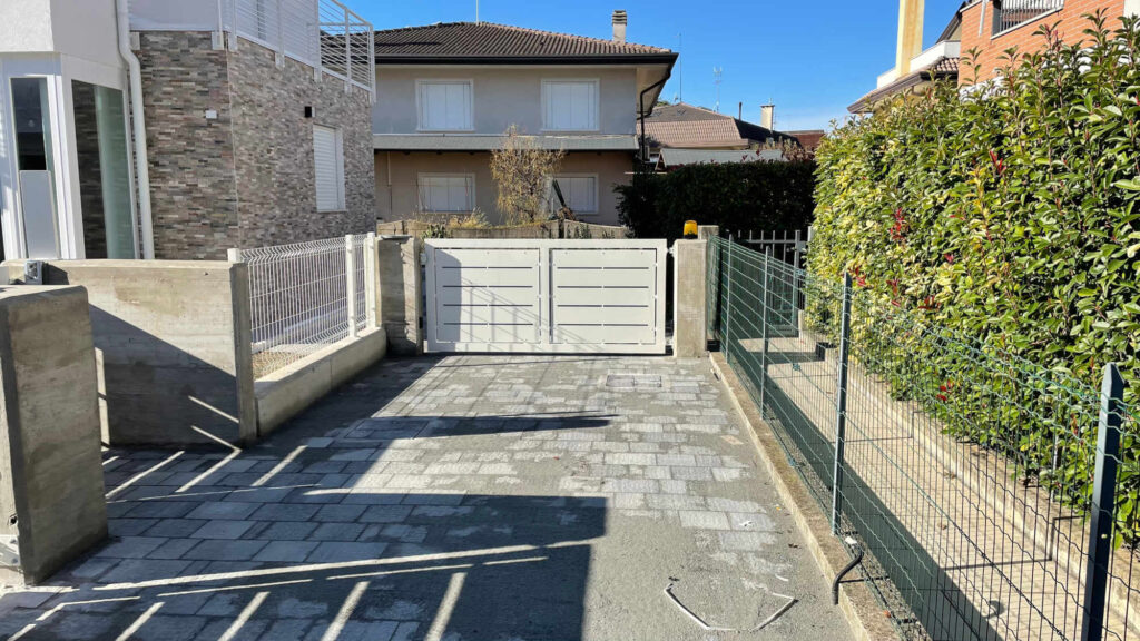 Cancello carraio scorrevole in metallo verniciato di bianco, con design a fasce orizzontali e leggere fessure, installato per chiudere un vialetto pavimentato