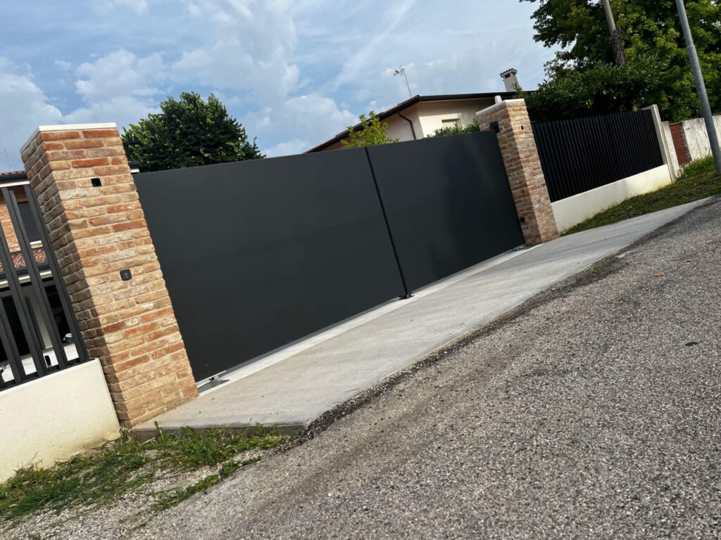 Cancello scorrevole moderno in lamiera cieca color antracite, progettato per garantire la privacy, montato tra due pilastri in mattoni faccia a vista