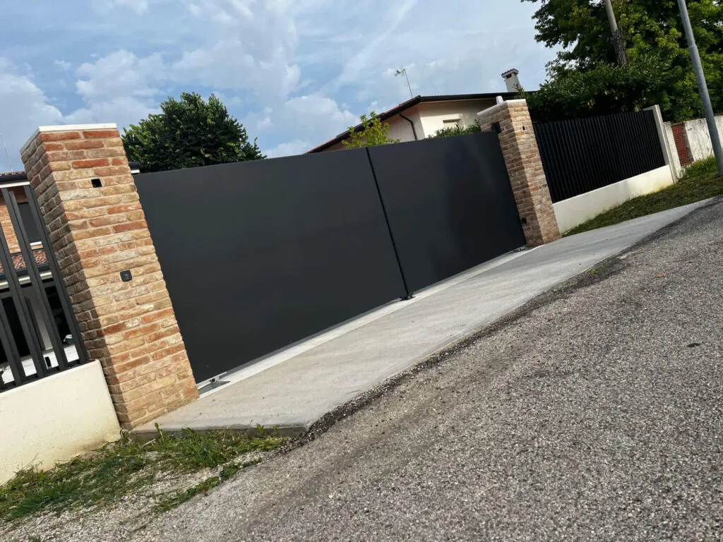 Cancello scorrevole moderno in lamiera cieca color antracite, progettato per garantire la privacy, montato tra due pilastri in mattoni faccia a vista
