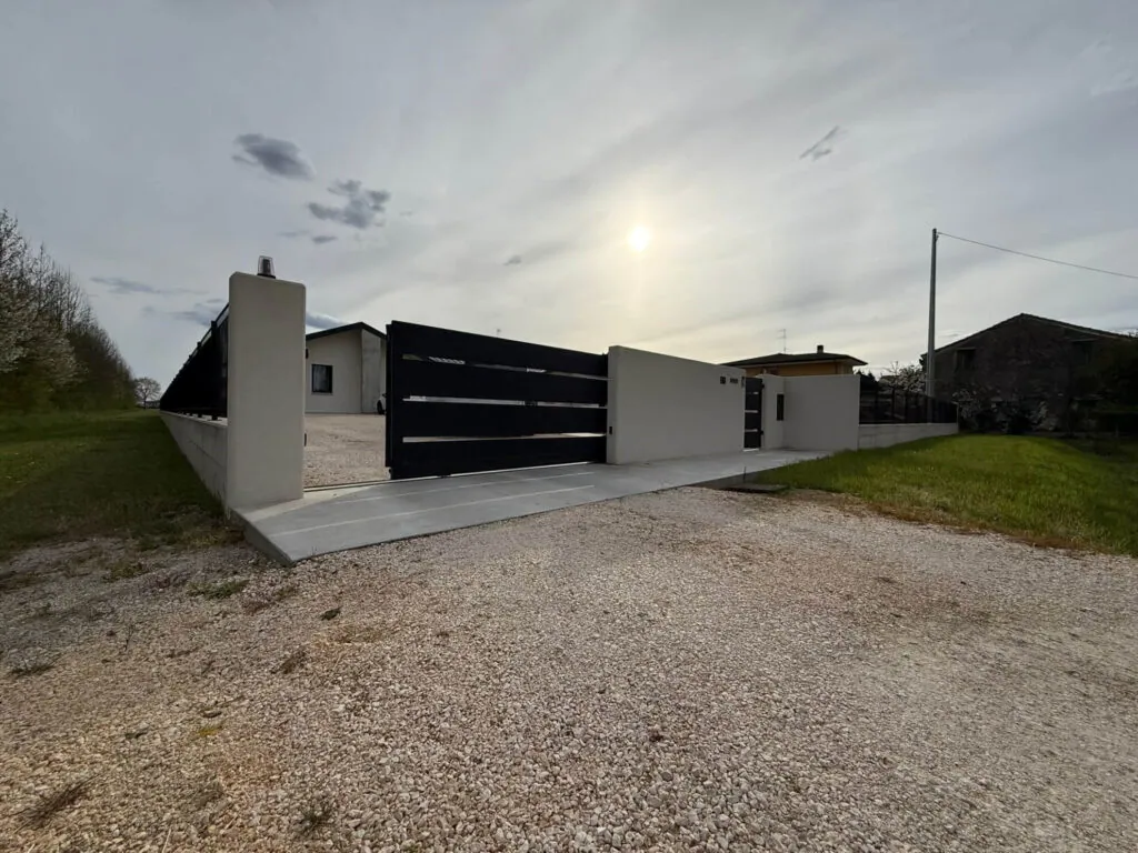 Cancello carraio scorrevole dal design moderno, realizzato in metallo nero a fasce orizzontali, inserito in un muretto di recinzione in cemento liscio - 2A Carpenteria