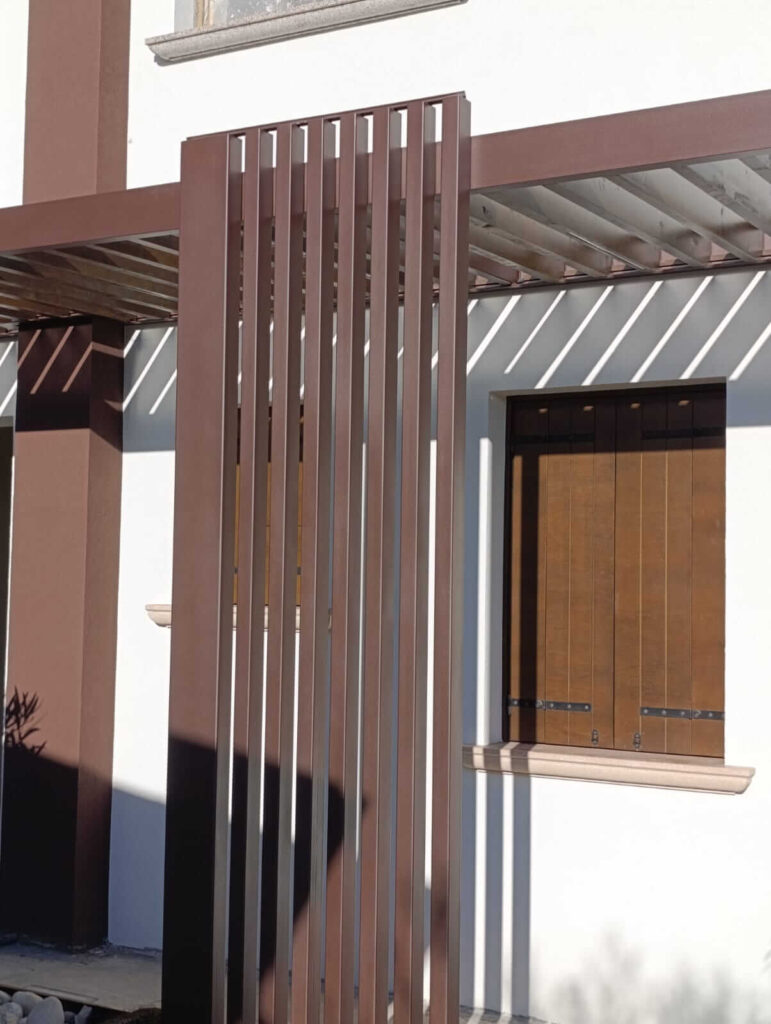Dettaglio ravvicinato dei listelli verticali in metallo che compongono il pilastro di una struttura frangisole (brise-soleil). Lavorazione di alta precisione per l'architettura d'esterni, progettata e installata da Carpenteria 2A.