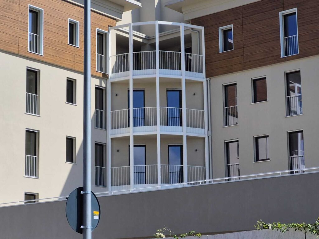 Strutture metalliche per ampi balconi e parapetti verniciati di bianco dal design lineare, installati sulla facciata di un moderno complesso residenziale. Opera di carpenteria per l'edilizia civile di Carpenteria 2A, operante in Veneto - Vista 4.