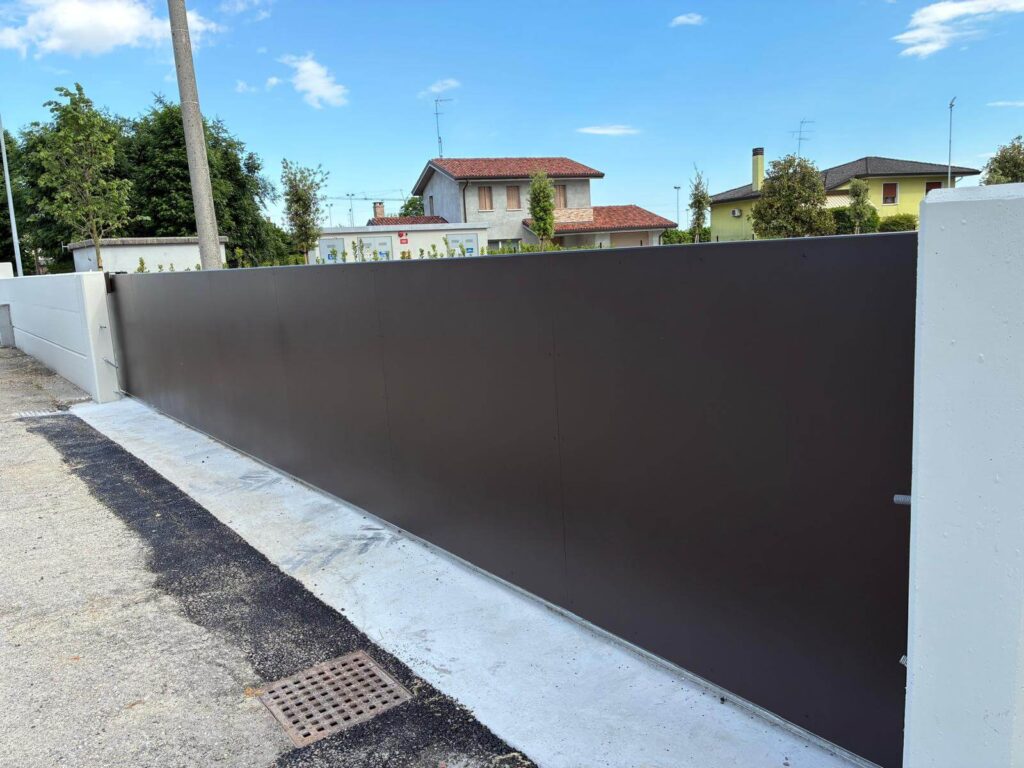 Lungo cancello carraio scorrevole dal design minimale, realizzato con pannelli ciechi in lamiera metallica nera per oscurare completamente la vista dall'esterno - Vista1