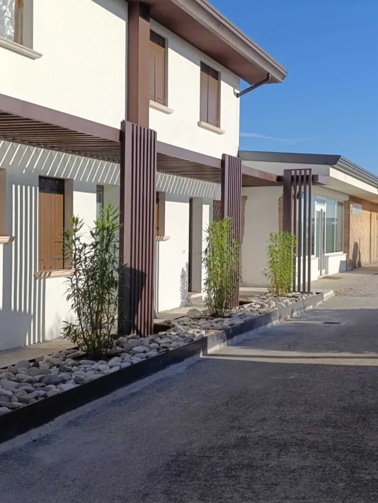 Lungo pergolato moderno in metallo marrone con funzione frangisole, addossato alla facciata di un edificio per creare zone d'ombra. Struttura architettonica per esterni realizzata su misura da Carpenteria 2A a Treviso, Veneto.