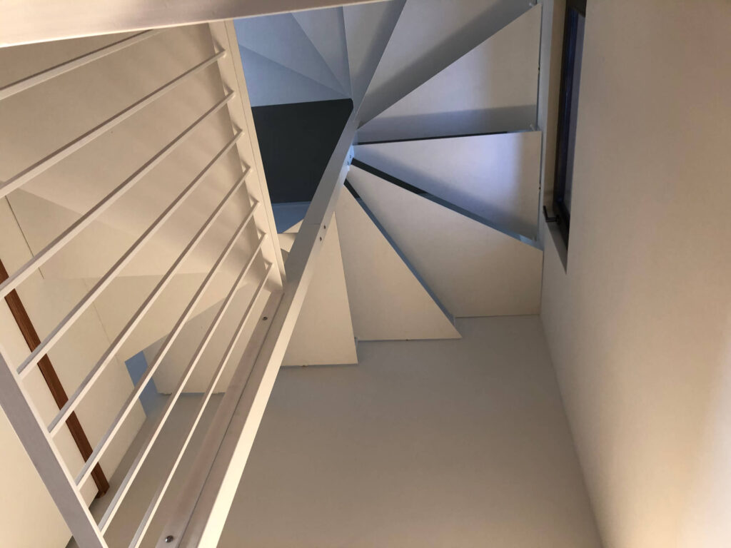 Vista dal basso di una scala a chiocciola moderna in metallo verniciato bianco, con parapetto a tondini. Realizzazione su misura per interni a cura di Carpenteria 2A, Treviso.