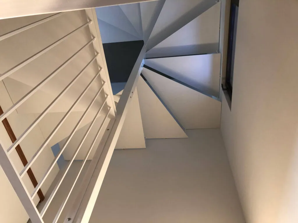 Vista dal basso di una scala a chiocciola moderna in metallo verniciato bianco, con parapetto a tondini. Realizzazione su misura per interni a cura di Carpenteria 2A, Treviso.