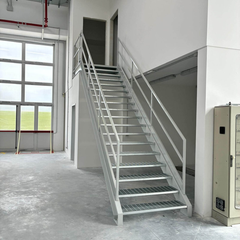 Scala industriale in metallo zincato e verniciato con gradini in grigliato antiscivolo e parapetto di sicurezza, per l'accesso al soppalco di un capannone. Struttura metallica progettata e posata da Carpenteria 2A a Treviso, Veneto.