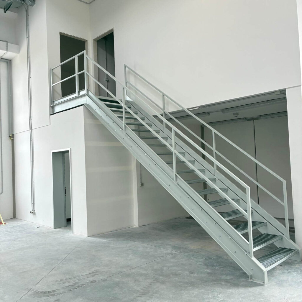 Scala industriale in metallo zincato e verniciato con gradini in grigliato antiscivolo e parapetto di sicurezza, per l'accesso al soppalco di un capannone. Struttura metallica progettata e posata da Carpenteria 2A a Treviso, Veneto - Vista 2.