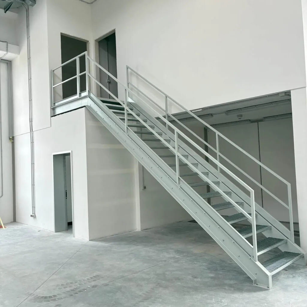 Scala industriale in metallo zincato e verniciato con gradini in grigliato antiscivolo e parapetto di sicurezza, per l'accesso al soppalco di un capannone. Struttura metallica progettata e posata da Carpenteria 2A a Treviso, Veneto - Vista 2.