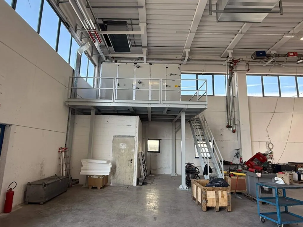 Struttura metallica portante a uso soppalco industriale, dotata di parapetto di sicurezza e scala d'accesso, progettata per sostenere un grande impianto di aerazione all'interno di un capannone. Opera di carpenteria pesante realizzata da azienda 2A a Treviso, Veneto.