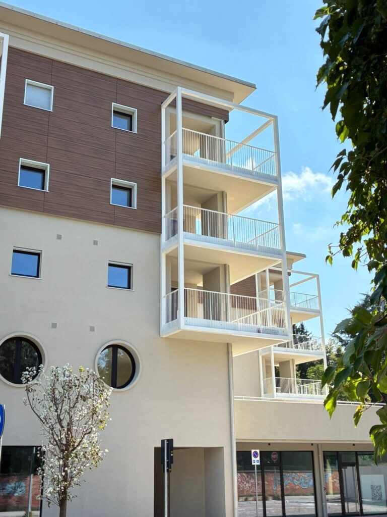 Strutture metalliche per ampi balconi e parapetti verniciati di bianco dal design lineare, installati sulla facciata di un moderno complesso residenziale. Opera di carpenteria per l'edilizia civile di Carpenteria 2A, operante in Veneto - Vista 2.
