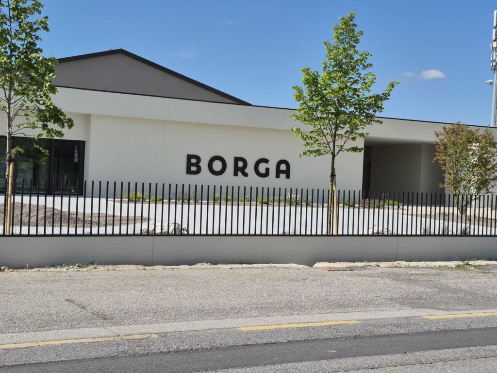 Facciata dell'edificio aziendale Borga parzialmente completato, con la scritta nera ben visibile e giovani alberi piantati lungo il perimetro